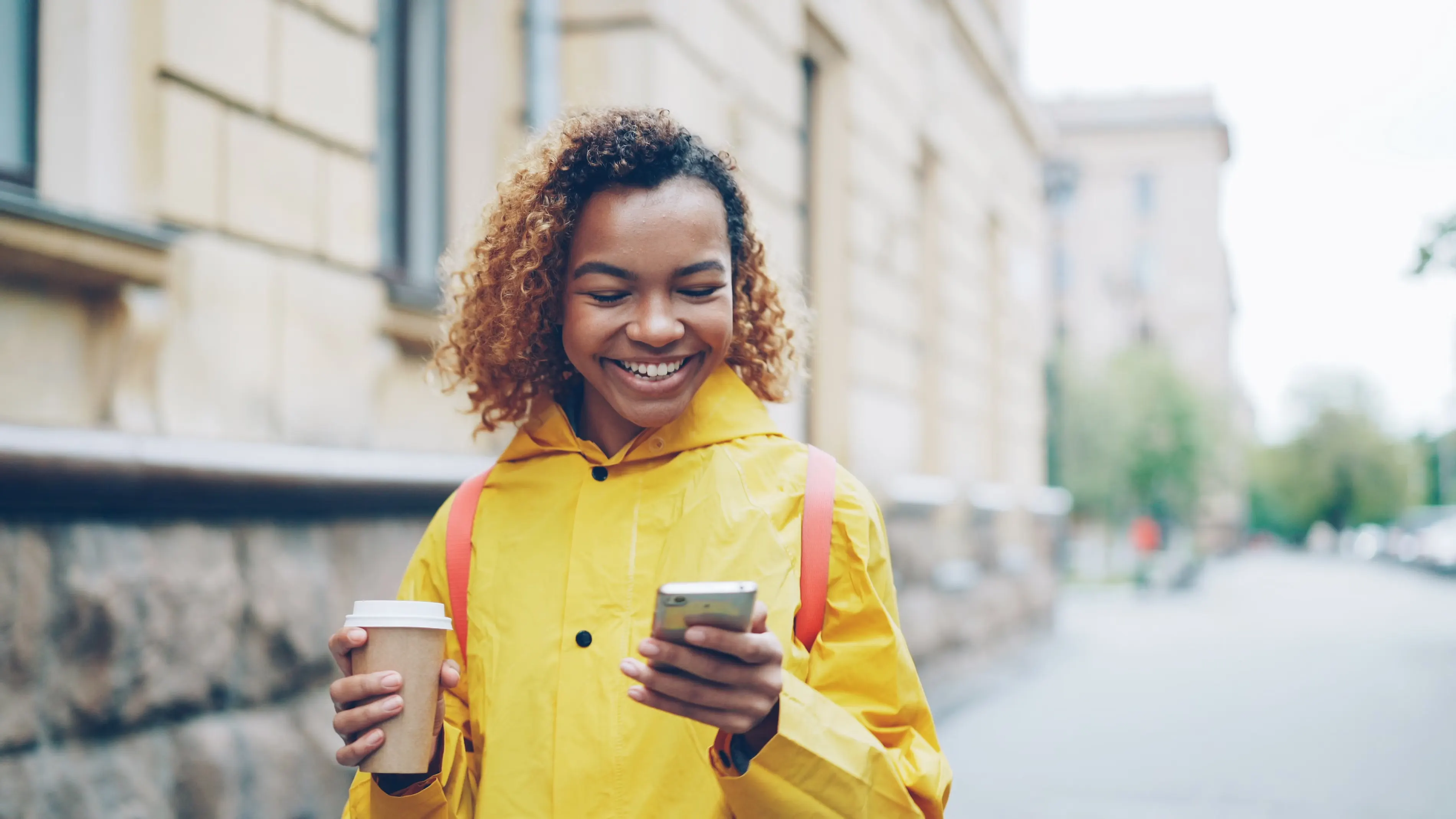 Smilende kvinne med mobiltelefon og kaffekopp i byen